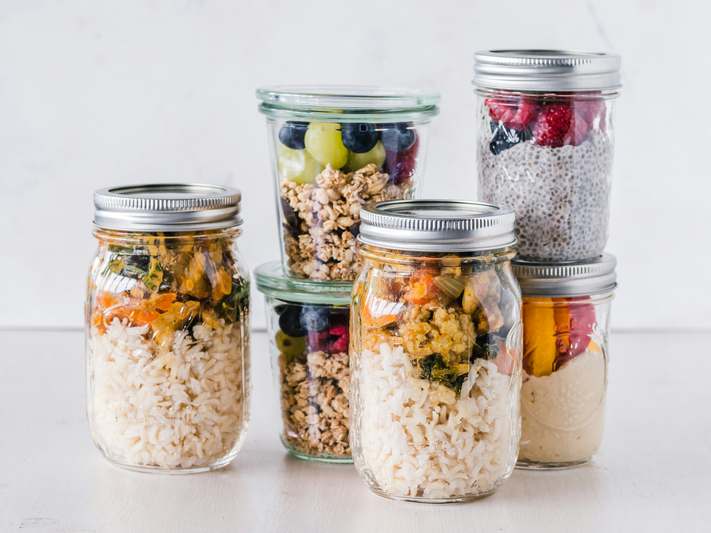 Two diverse hands placing fresh produce into glass meal prep containers on a clean kitchen counter