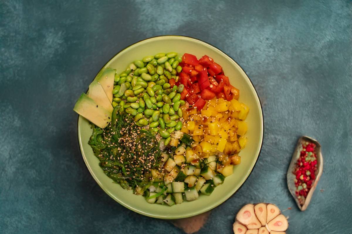 rainbow veggie container filled with red bell pepper, orange carrot, yellow squash, green broccoli, blue-purple cabbage, and brown quinoa